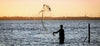 A man throwing a net into the ocean, hoping to catch some fish. 